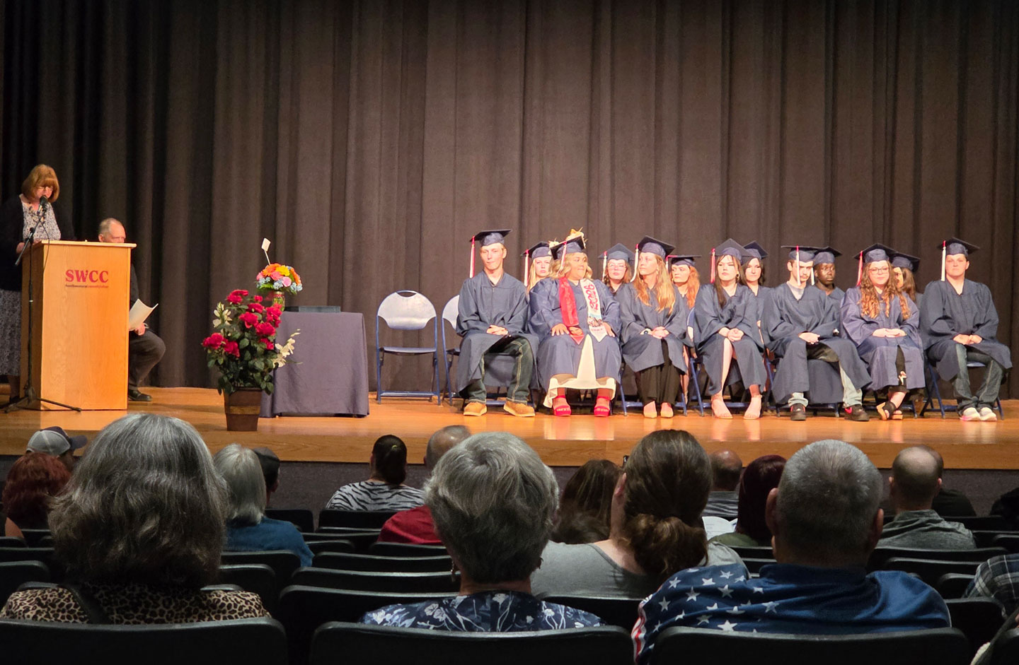 2025-26 HSED grads on stage in gowns with speaker at podium