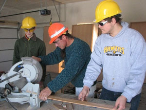Students with hardhats using a miter saw to cut wood trim