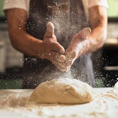 Chef's hands spraying flour over the dough