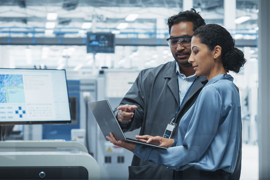 Two people working on a laptop standing in a technology factory environment.