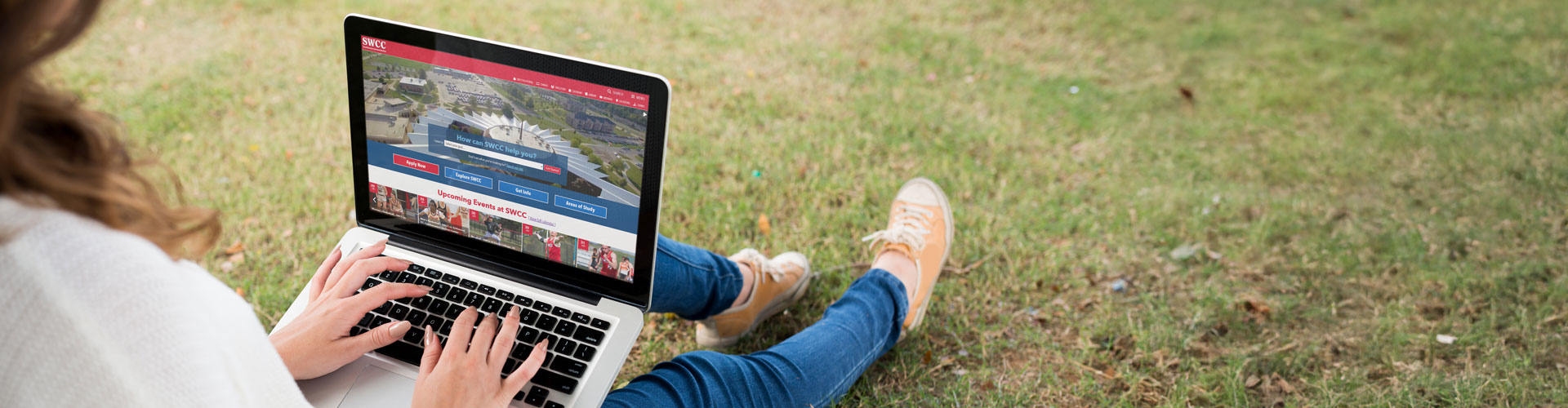 student sitting in the grass using a laptop with the SWCC Website on the screen
