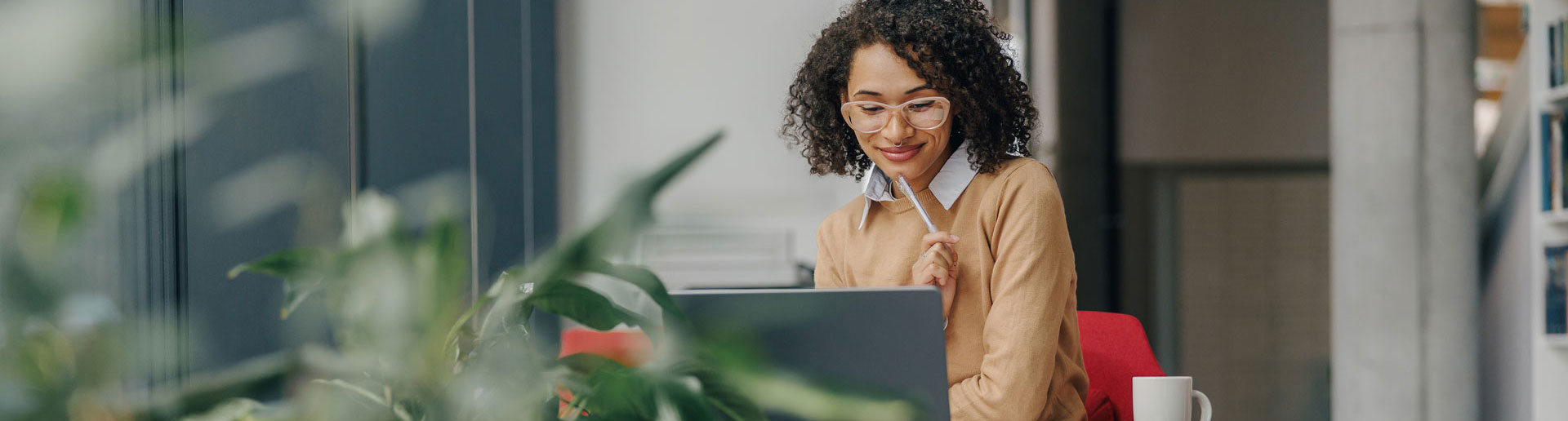Stylish woman in eyeglasses working on laptop while sitting near window