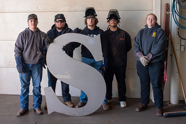 Welding students standing with the SWCC "S"