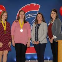 Students standing with medals taking a photo some employees in front of a Spartan backdrop